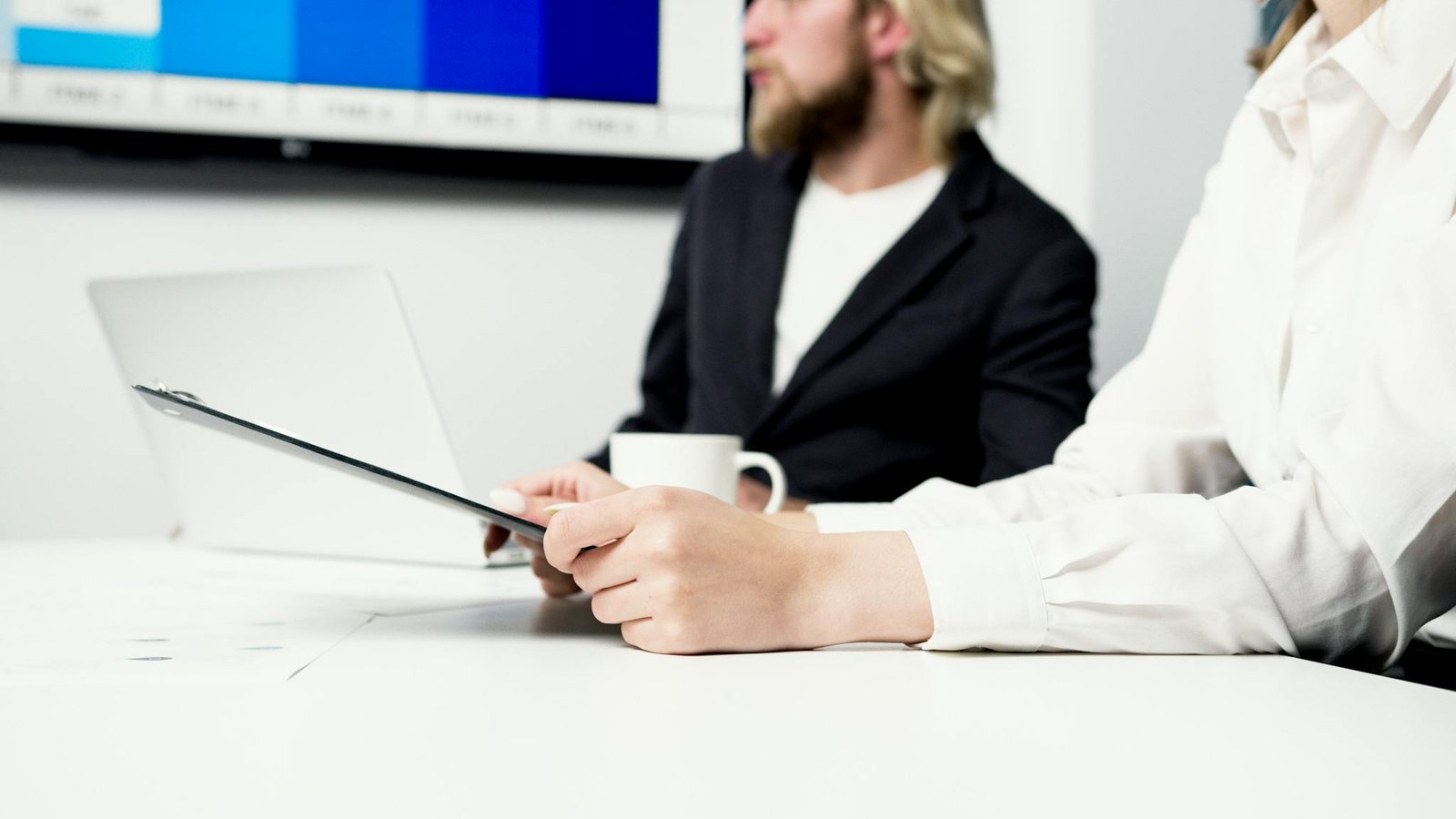 Professionals collaborating at a meeting with a laptop and clipboard in a corporate setting.